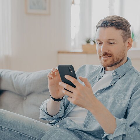 Junger Mann, der auf der Couch sitzt und im Internet surft